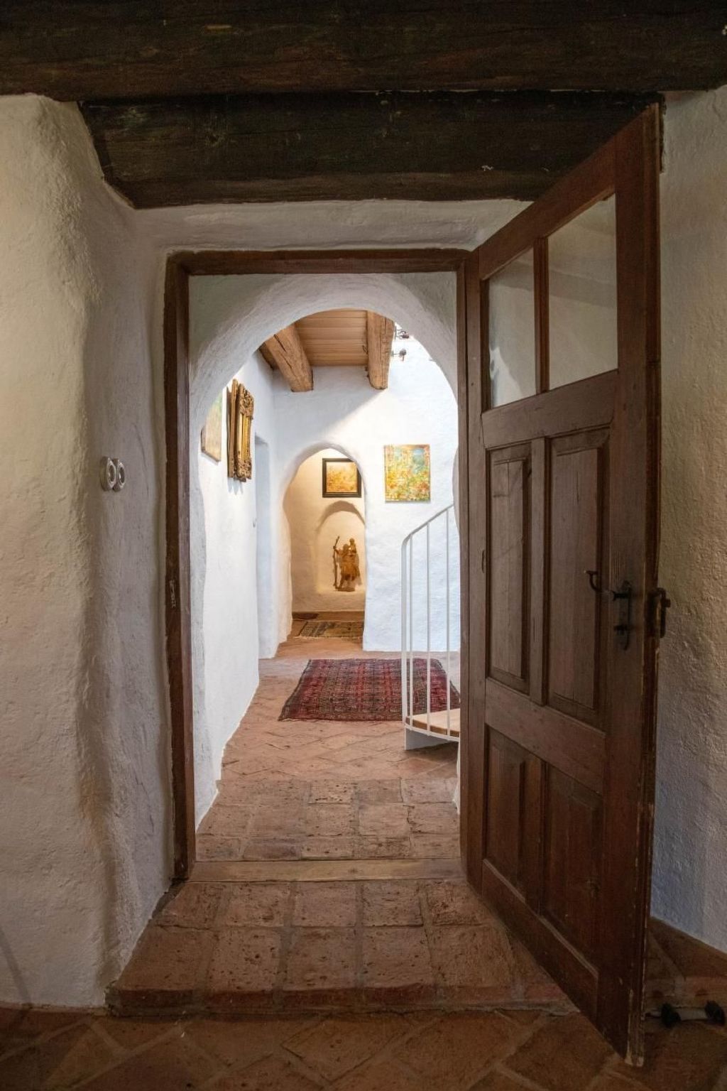 A hallway with a wooden door, white walls, and a tiled floor leading to a room with a dog statue.
