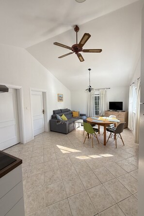 A spacious living area with a ceiling fan, a dining table with chairs, a sofa, and a television. - Wohnung Vir 02 in Strandnähe - Agentur TA Leut by Interhome (Vir)