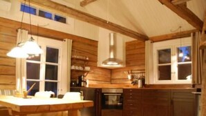 Un intérieur en bois comprenant un espace cuisine, avec une table et des chaises, un poêle et des placards.