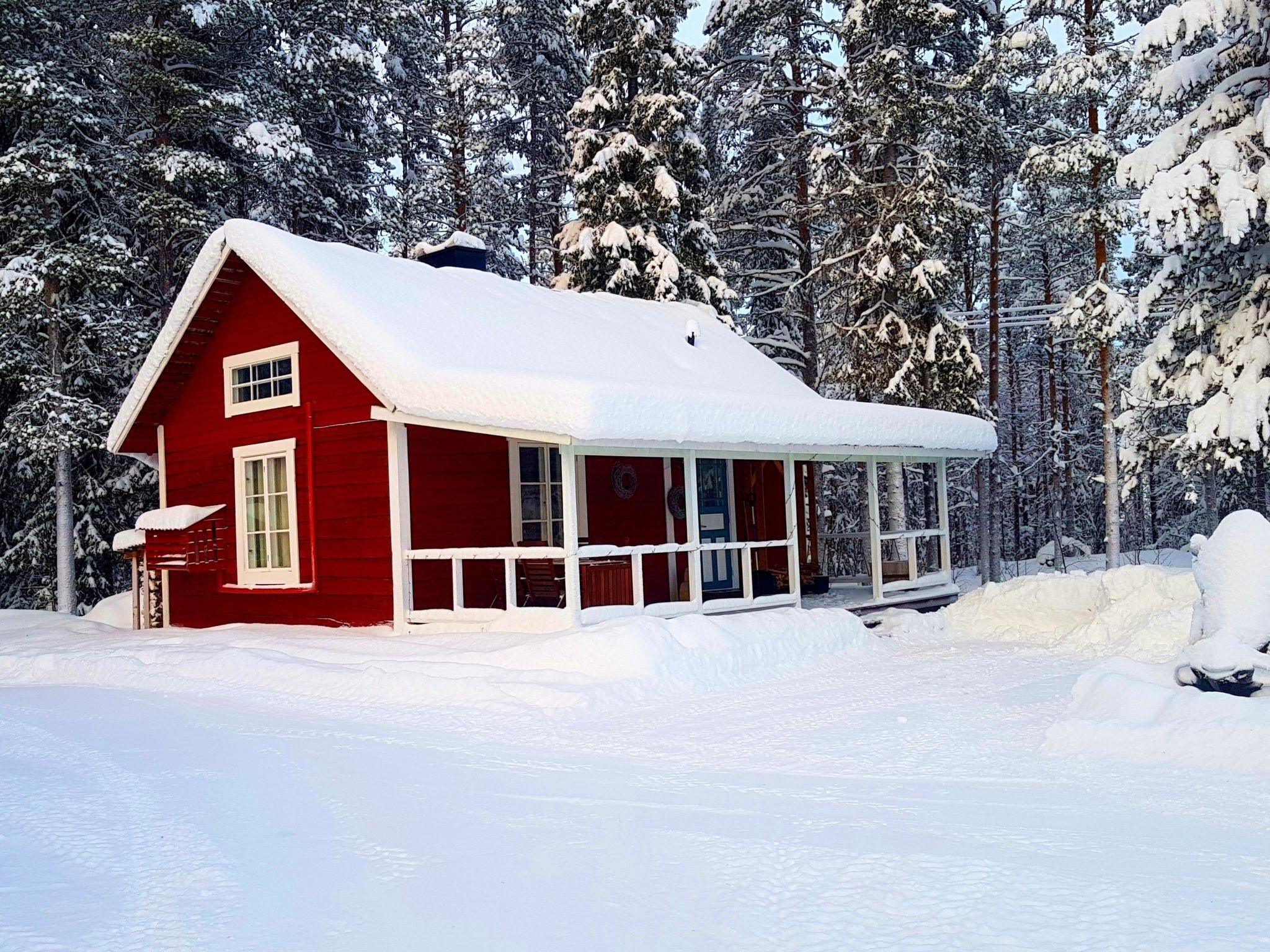 Eine rote Holzhütte mit einer Laube, umgeben von schneebedeckten Bäumen.