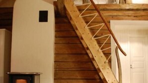 Un escalier en bois mène à une mezzanine où se trouvent un poêle à bois et un panier de bois de chauffage.