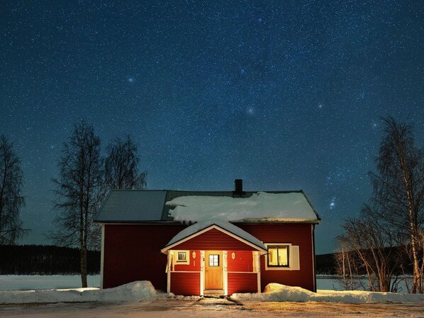 A red cabin with a snow-covered ground, a clear night sky, and a visible starry sky.