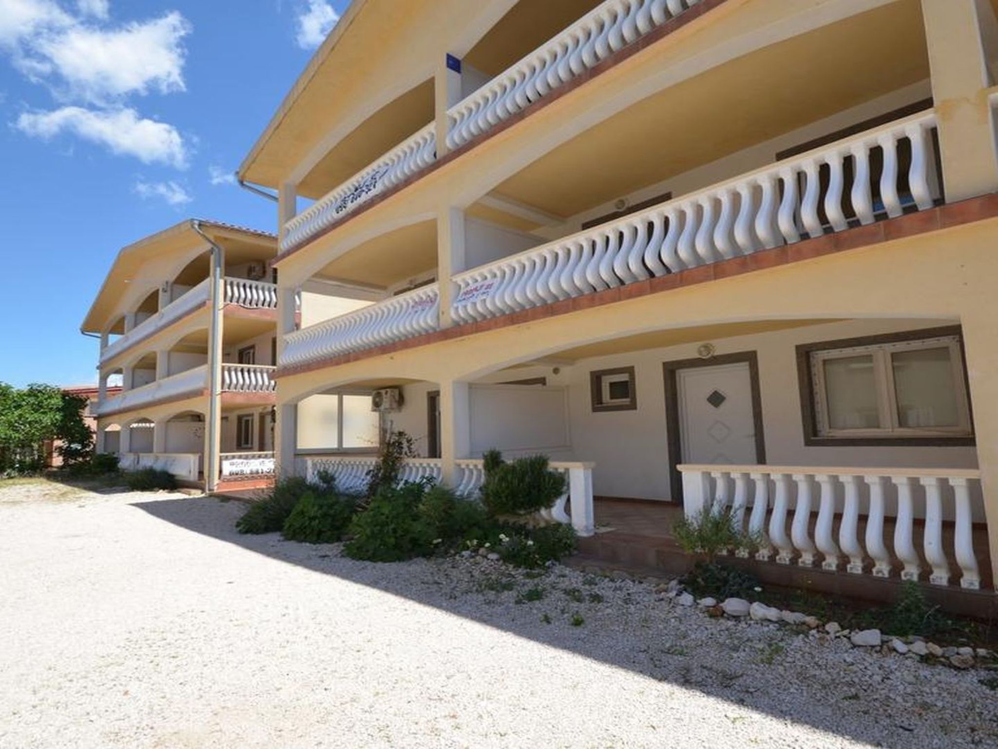 Ein mehrstöckiges Hotel mit Balkonen, einer Schotterzufahrt und einem klaren Himmel.