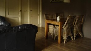 A room with a black leather sofa, a wooden dining table with wicker chairs, and a hanging light fixture. - Unterbringung Ganzekuken by Interhome (Vriescheloo)