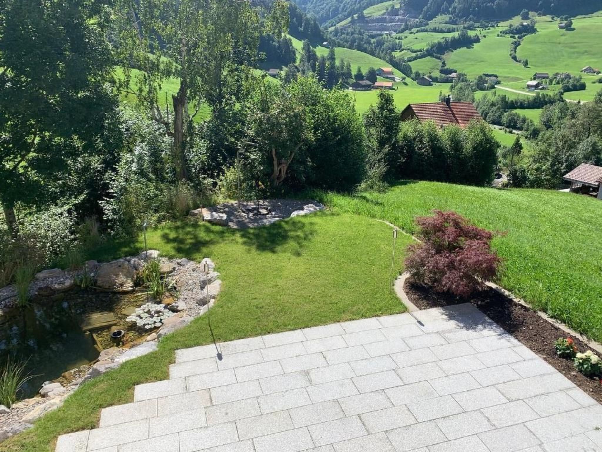 Une terrasse en pierre mène à un espace verdoyant agrémenté d’un petit étang et de quelques arbres.