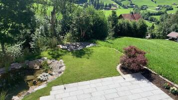 Une terrasse en pierre mène à un espace verdoyant agrémenté d’un petit étang et de quelques arbres.