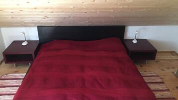 Ein Schlafzimmer mit rotem Bettbezug, einem Holz-Kopfteil, zwei Nachttischen mit Lampen und einem gemusterten Teppich.