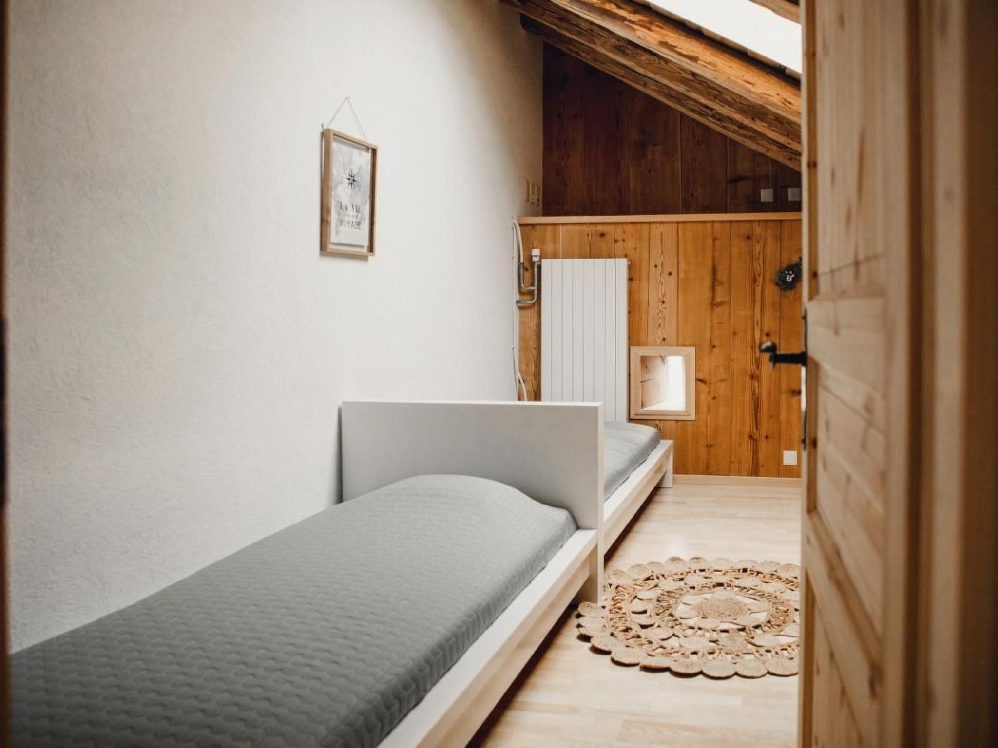 Une petite chambre à coucher, chaleureuse et accueillante, avec un lit simple, une porte en bois et une petite fenêtre.