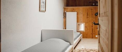 Une petite chambre à coucher, chaleureuse et accueillante, avec un lit simple, une porte en bois et une petite fenêtre.