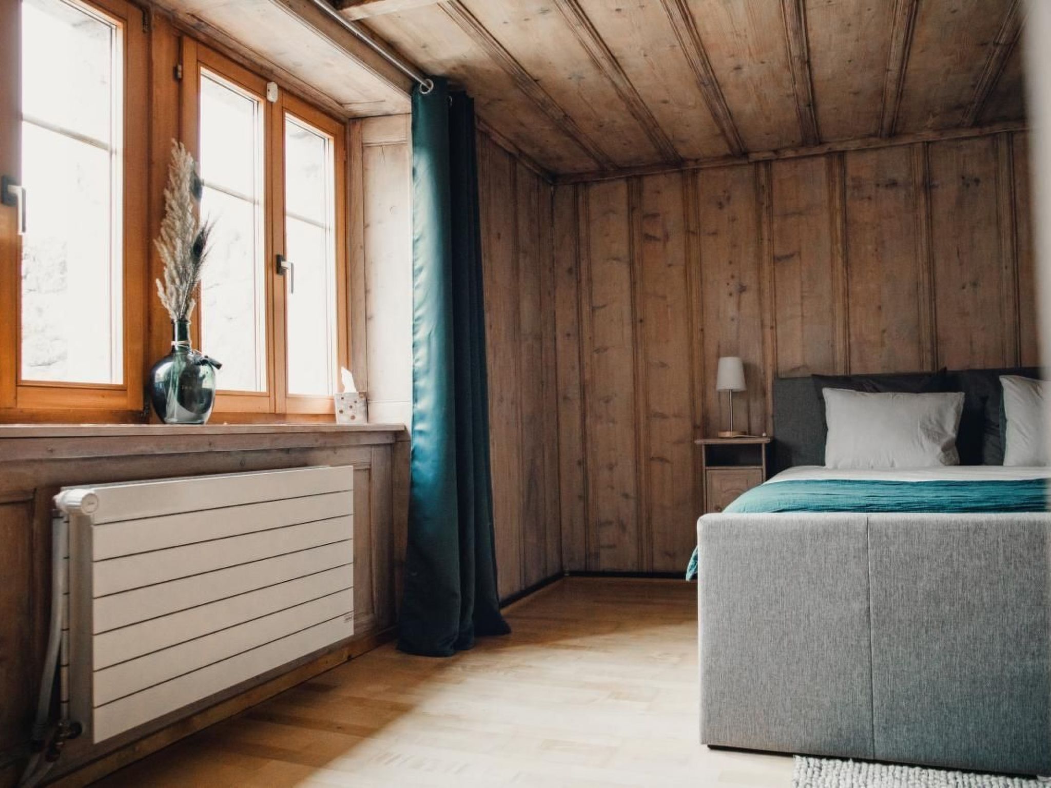 A bedroom with wooden walls, a bed, a nightstand, a lamp, and a window with curtains.