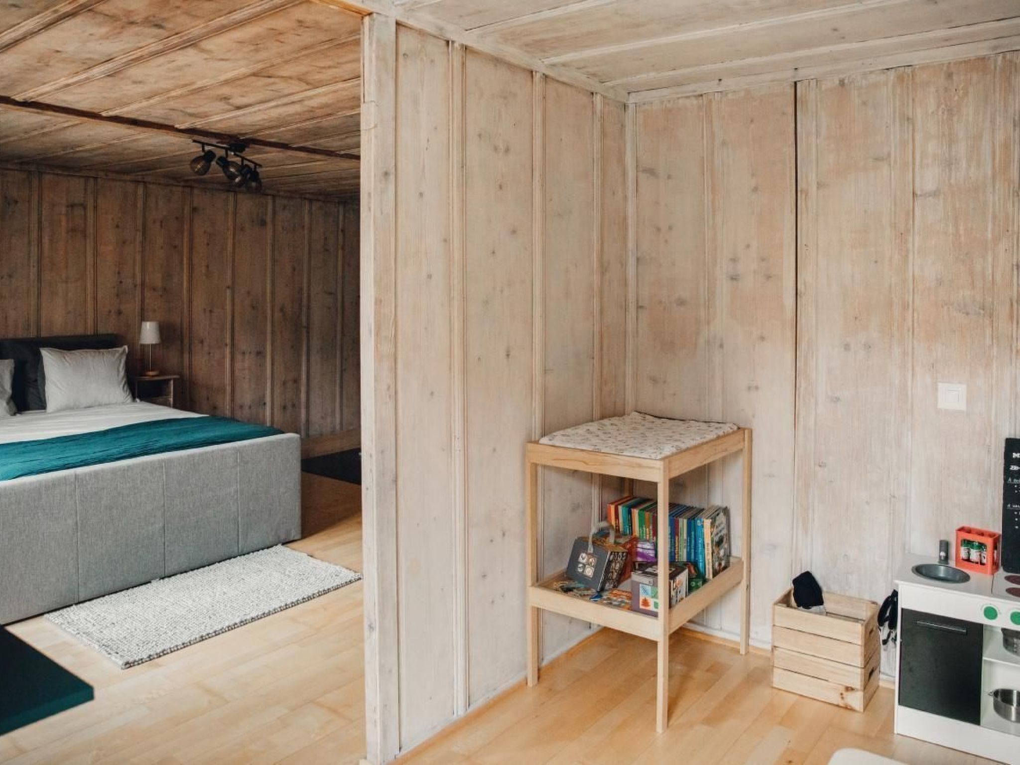 Une chambre avec un lit, une petite étagère en bois remplie de livres et un coin cuisine.