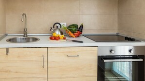 Una cocina moderna con un lavamanos de acero inoxidable, un hervidor, una tabla de cortar con verduras y un horno empotrado.