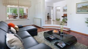 En moderne stue med en sort lædersofa, et glasbord og udsigt til et spiseområde gennem et stort vindue.