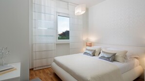 Et moderne soveværelse med en stor seng, et sengebord, en lampe og et vindue med lette gardiner.