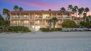 Een hotel aan het strand met meerdere balkons, palmbomen en een zandstrand.