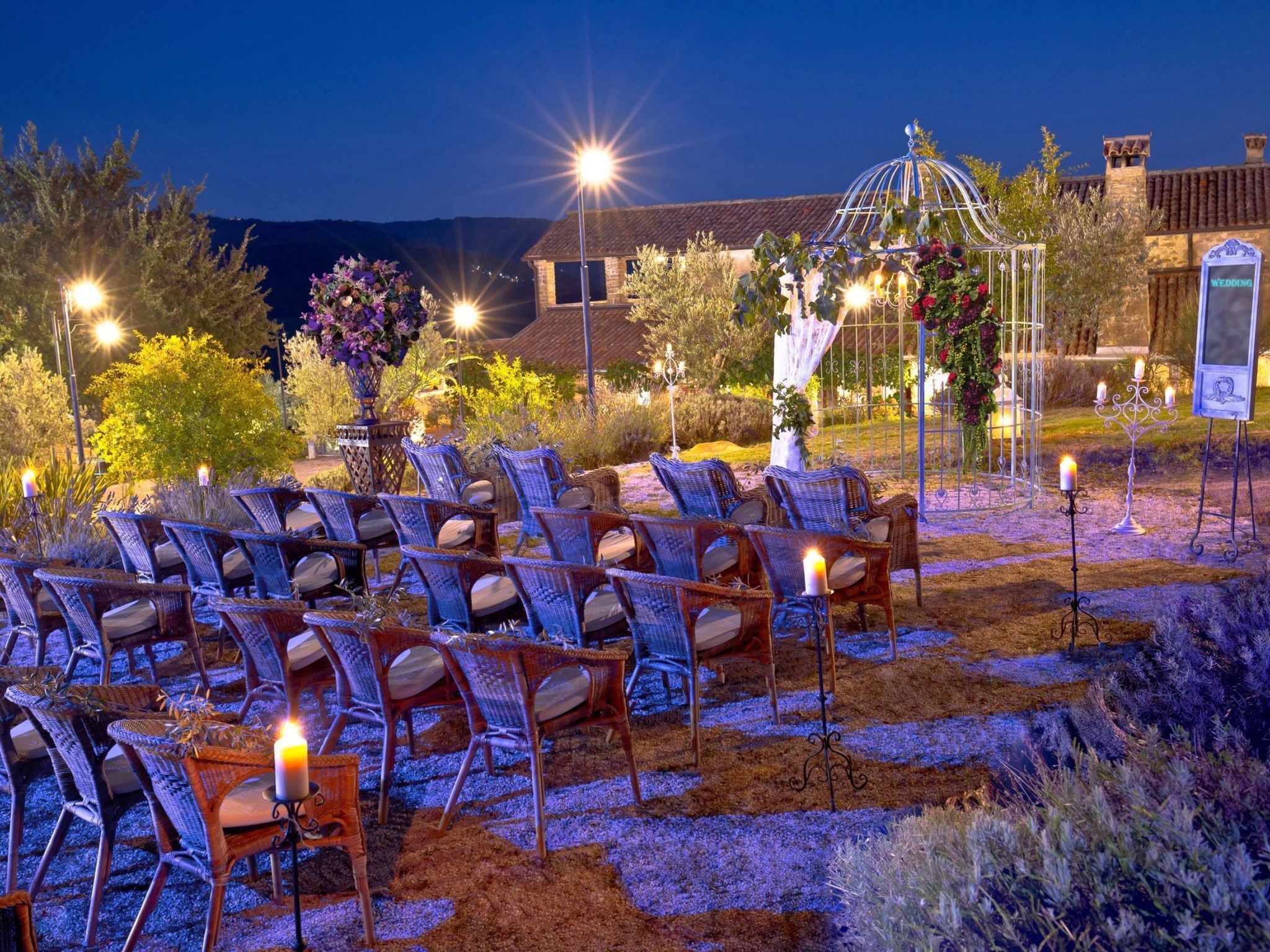 An outdoor seating area with wicker chairs and candles, surrounded by plants and a decorative gazebo.