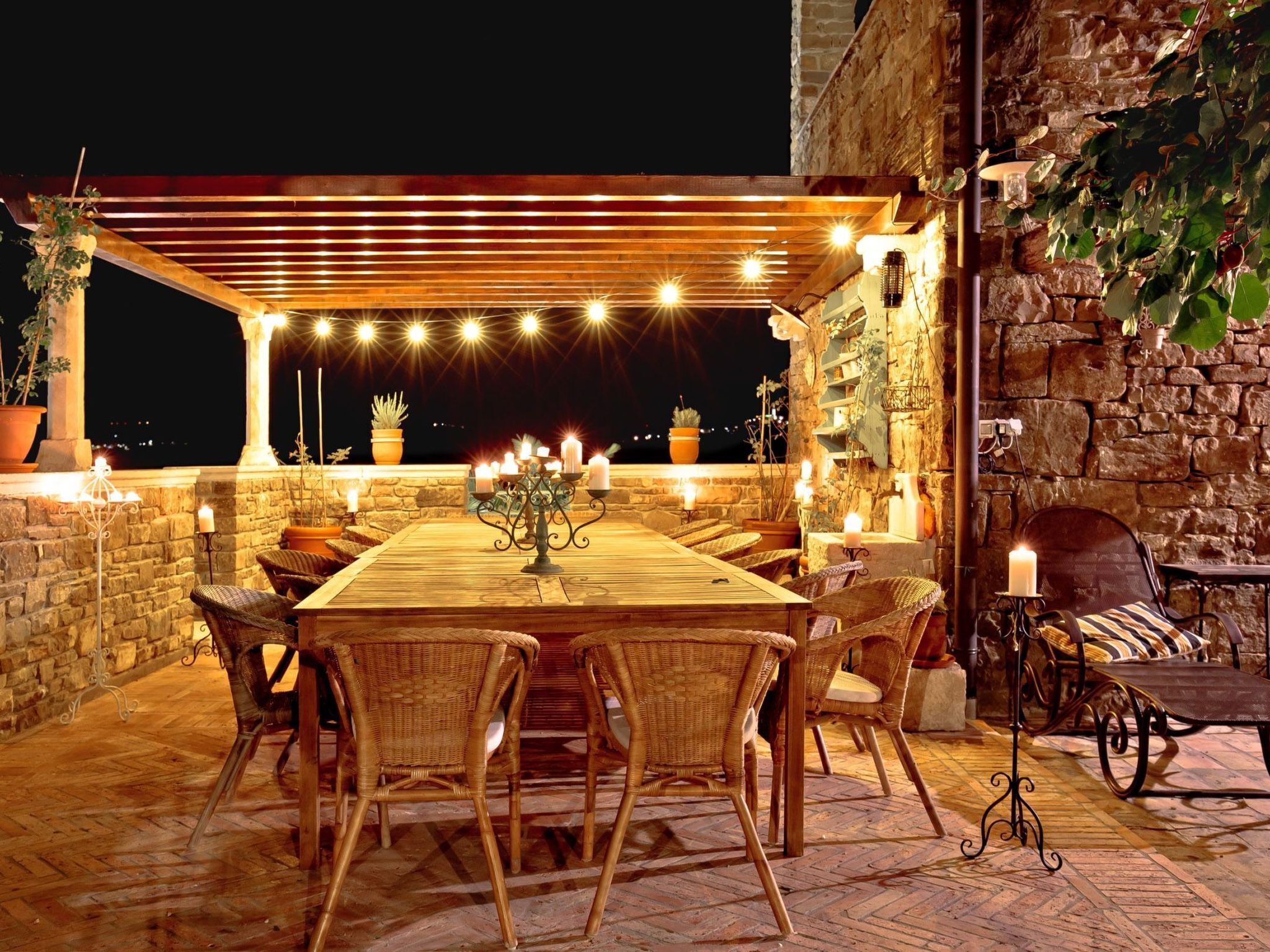 An outdoor dining area with a pergola, stone walls, and potted plants.