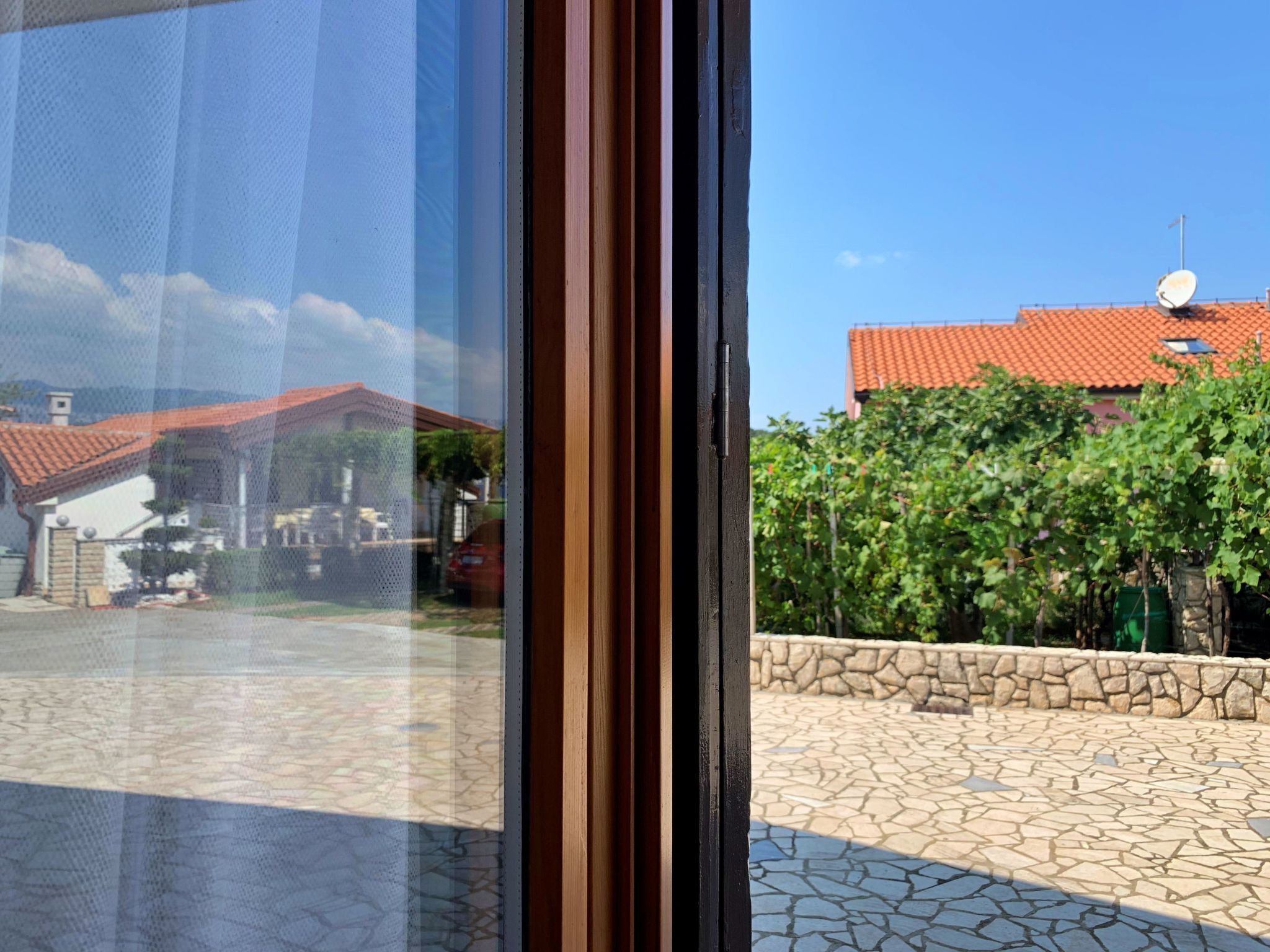 A view through a window with a stone patio and a red-tiled roof building in the background.