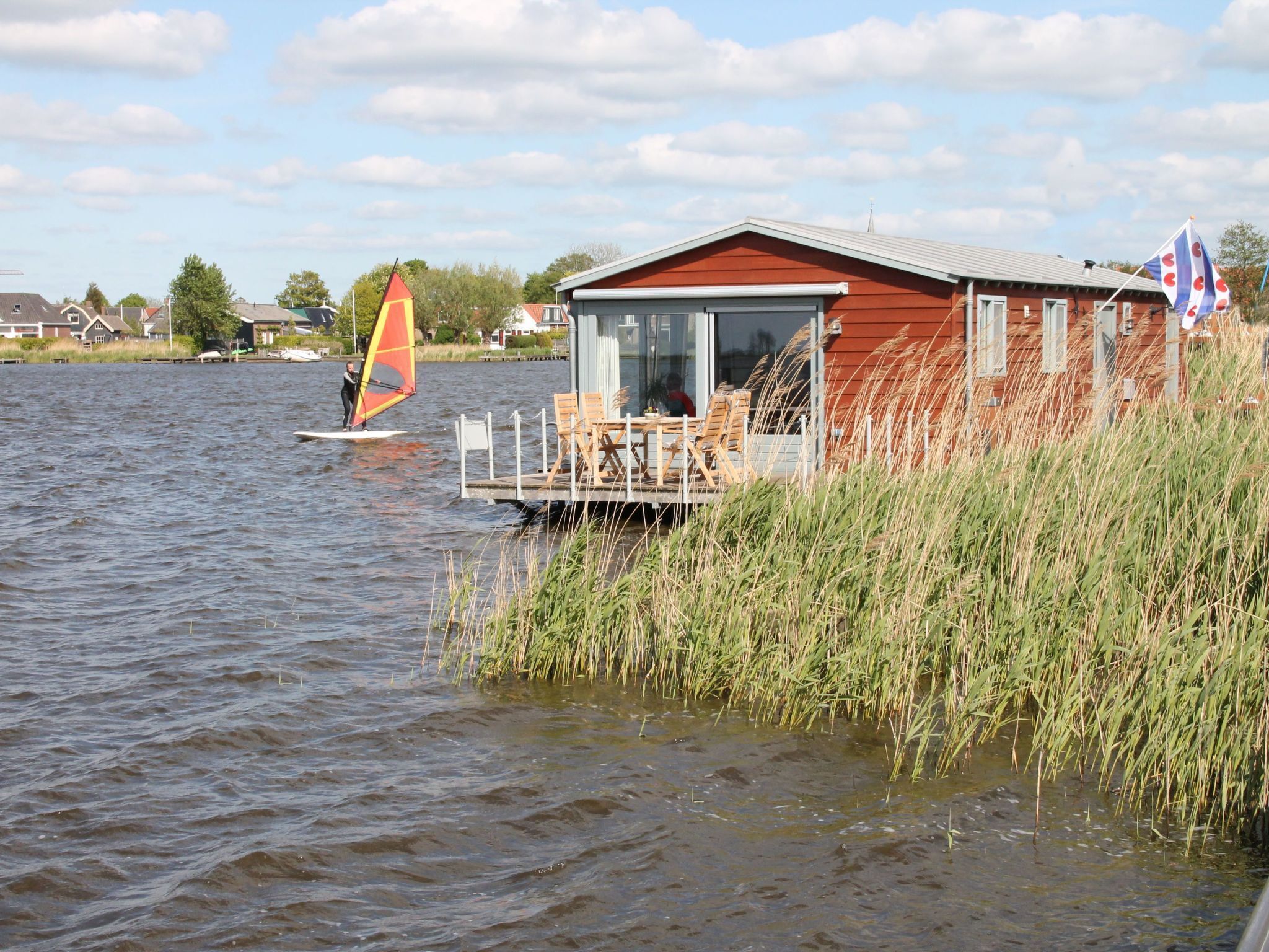 A lakeside building with a dock extending into the water, surrounded by tall grass.