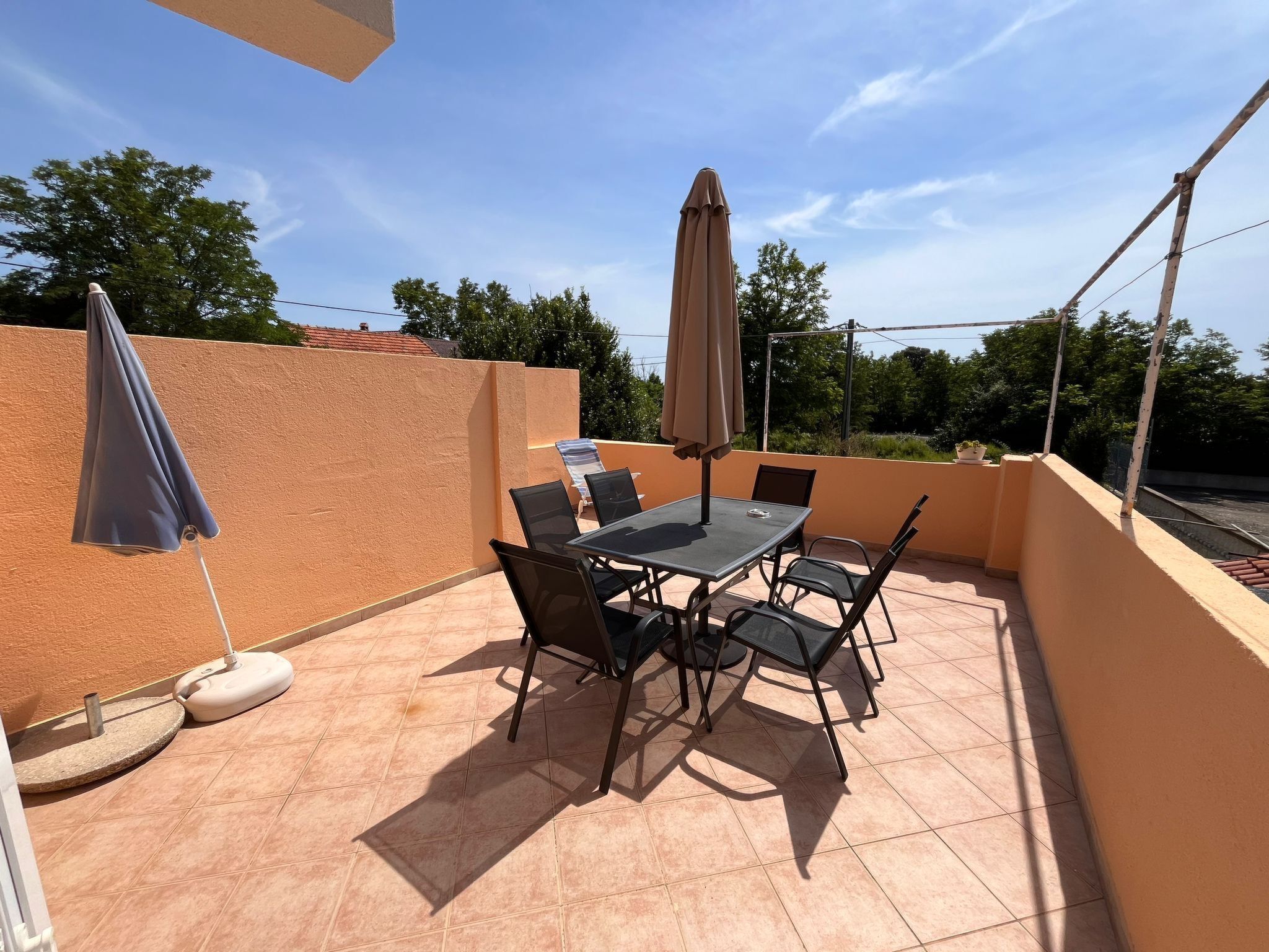 Un patio con tavolo e sedie, due ombrelloni e un pavimento piastrellato.