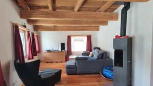 Un salon chaleureux avec des poutres apparentes, un canapé gris, un fauteuil noir et une cheminée.