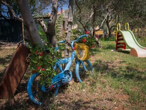 Ein blaues Fahrrad mit Korb, angelehnt an einen Baum in einem Park mit Spielplatz im Hintergrund.