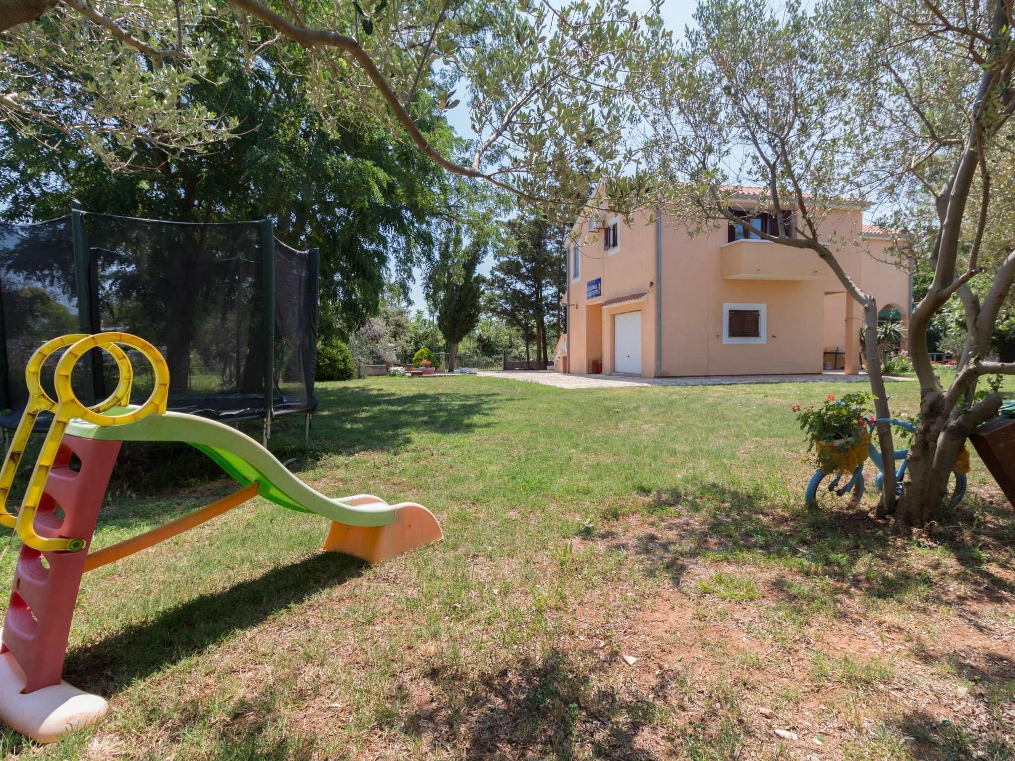 A playground with a slide and swings, surrounded by a grassy yard and trees.