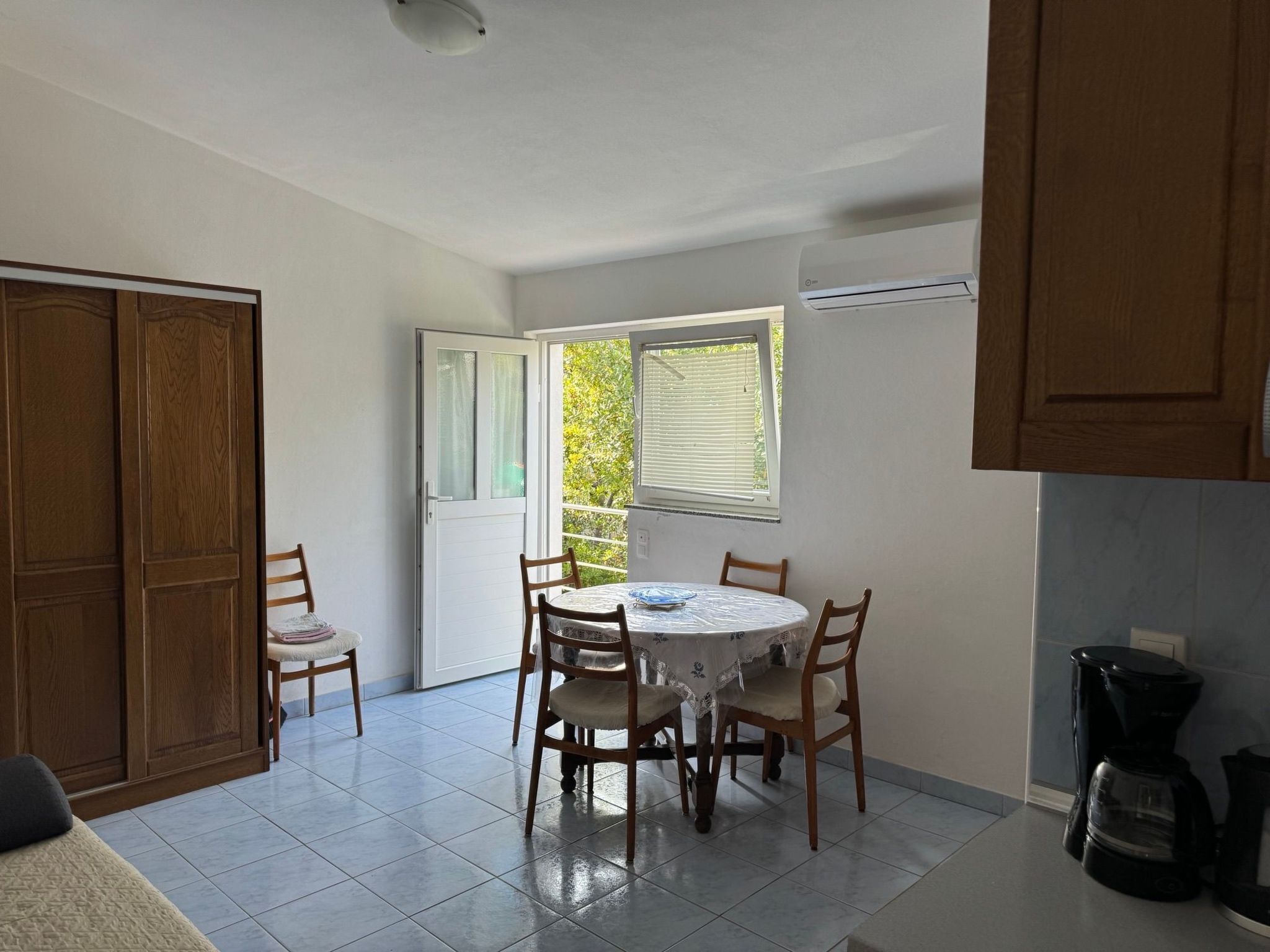A dining area with a round table and four chairs, a sliding door, and a window with blinds.