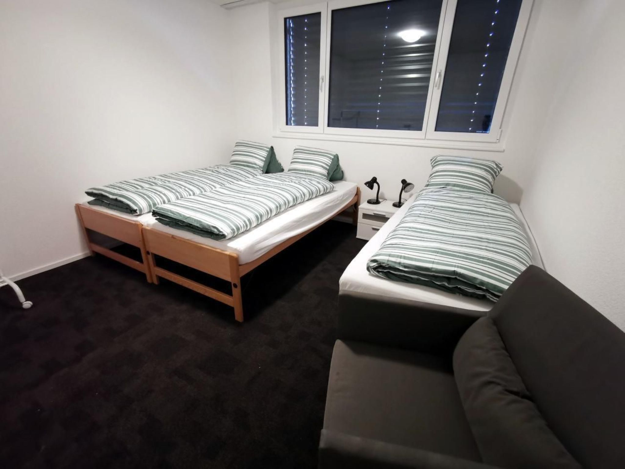 Une chambre avec deux lits simples, un petit bureau avec une lampe et un canapé.