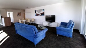 A modern living room with two blue sofas, a glass coffee table, a flat-screen TV, and a dining area with a table and chairs. - HIRSCHEN by Interhome (Gossau SG)