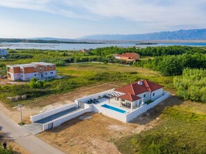 Ein modernes Haus mit Pool, umgeben von üppiger Vegetation und Blick auf See und Berge.