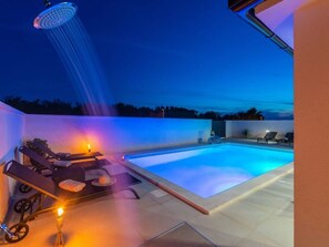 Ein moderner Poolbereich im Freien mit Whirlpool, Liegestühlen und einer Deckenbrause.