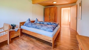 Quarto com cama de madeira, mesa de cabeceira, guarda-roupa de madeira e porta que dá para outro cômodo.