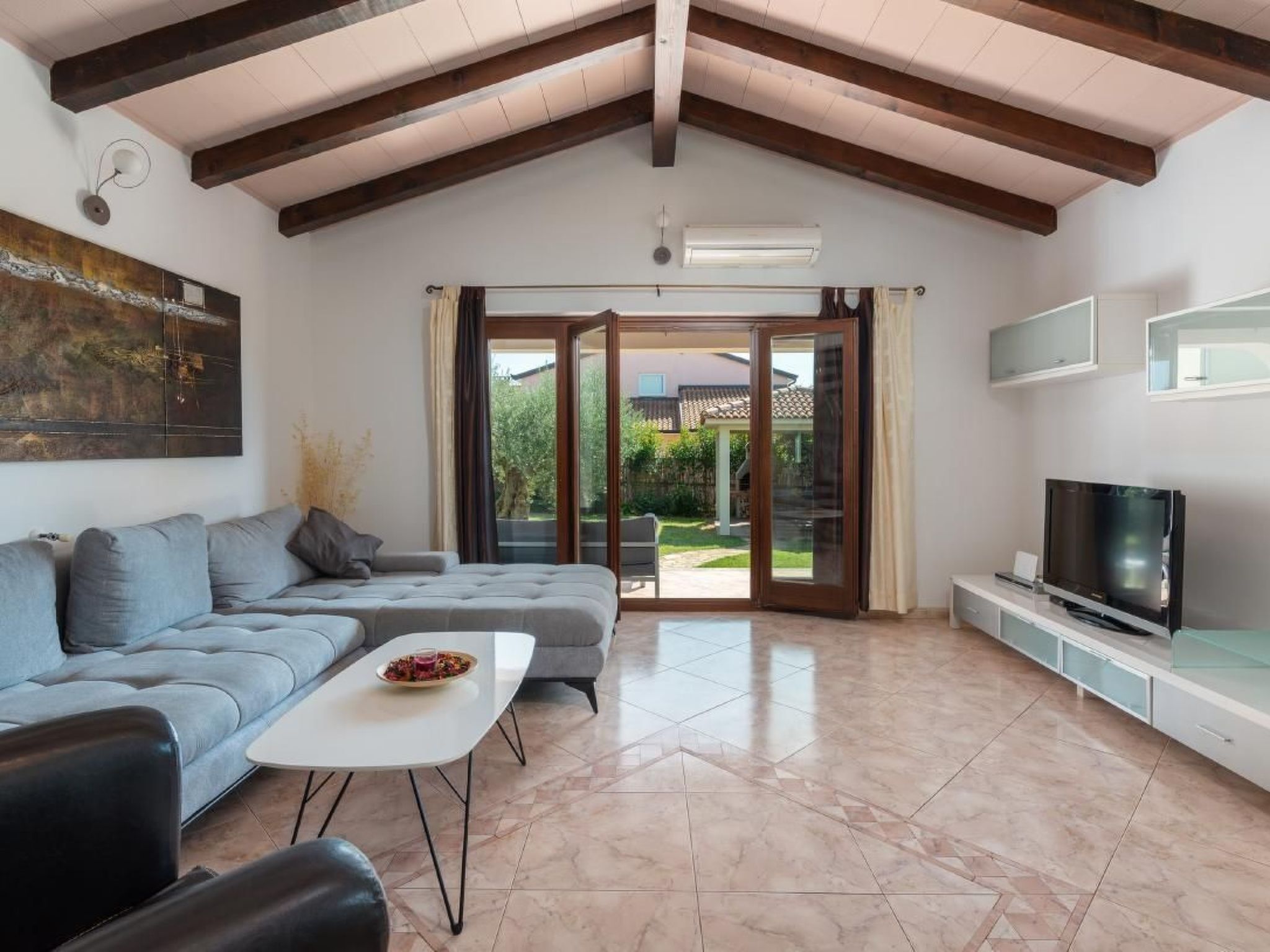 Un salon comprenant un canapé, une table basse, un téléviseur à écran plat et une porte-fenêtre coulissante donnant sur un jardin.