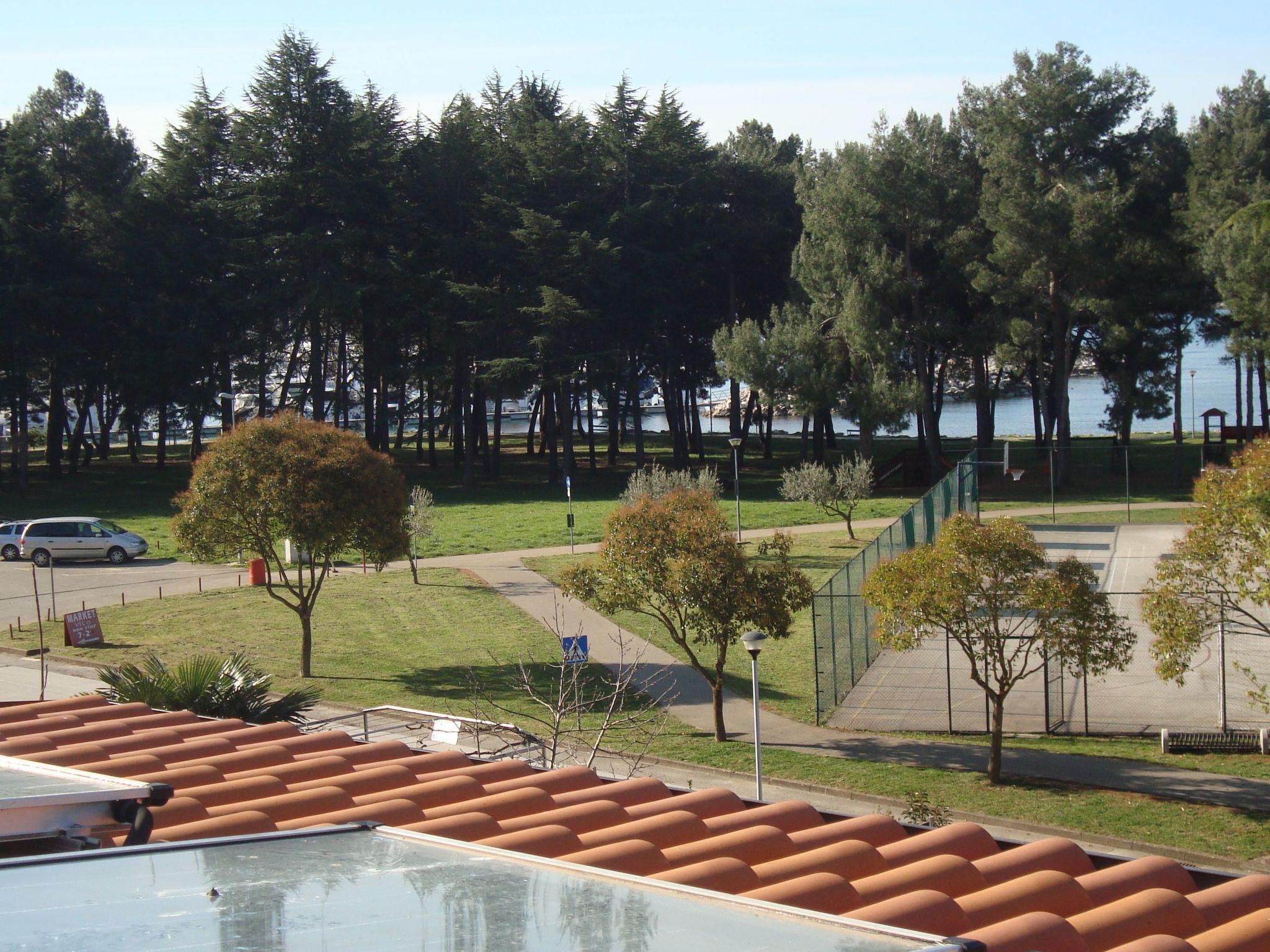 A park with a basketball court, trees, and a body of water in the background.