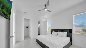 Un dormitorio moderno con una cama grande, un ventilador de techo y vistas a un paisaje verde a través del ventanal.