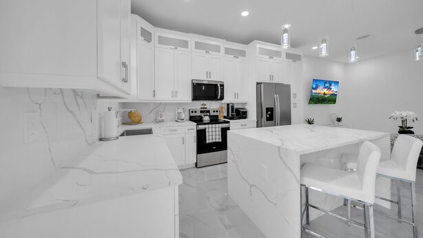 Una cocina moderna con armarios blancos, una isla central, electrodomésticos de acero inoxidable e iluminación colgante.