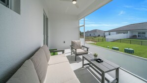 Balcón con sofá, sillón y mesa, con vistas a una zona residencial con casas y jardín.