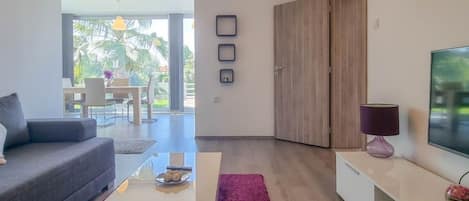 A modern living room with a grey sofa, a coffee table, a TV on a white stand, and a wooden wardrobe.