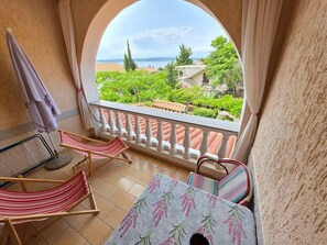 A balcony with a view of greenery and buildings, a table with a floral tablecloth, and two striped hammocks. - Appartement mit Balkon - gemeinsamer Pool und Terrasse by Interhome (Novi Vinodolski)