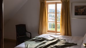 A bedroom with a bed, a chair, a window with curtains, and a painting on the wall.