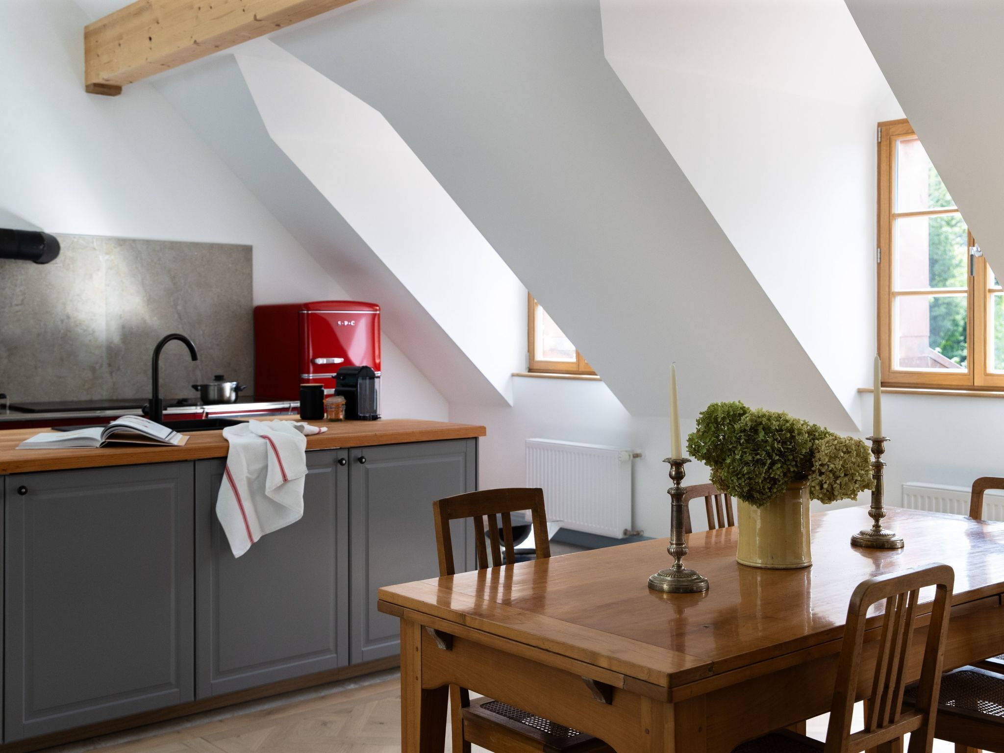 Una cucina con un tavolo e sedie in legno, una macchina del caffè rossa e una finestra che si affaccia sul verde.