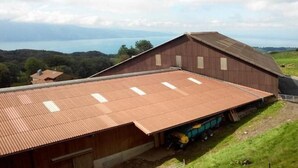 Um amplo edifício industrial com telhado de metal corrugado, localizado numa área rural com vista para um lago e colinas ao fundo.
