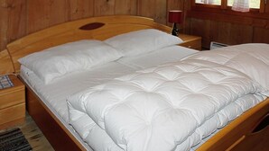 A wooden bed with white bedding in a room with wooden walls and a window with curtains.
