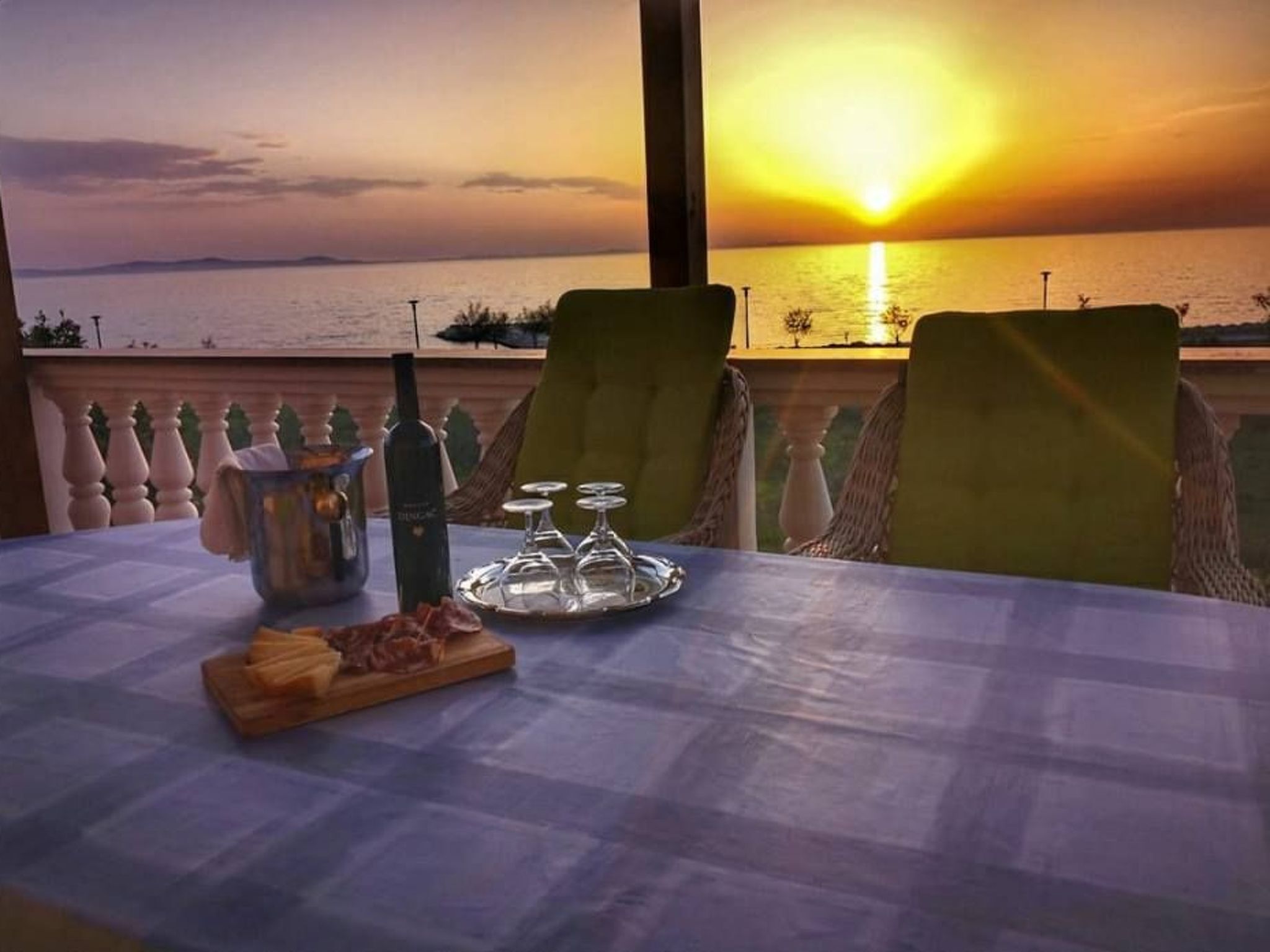 A table set for two with a view of the sunset over the sea, a bottle of wine, and a plate of food.