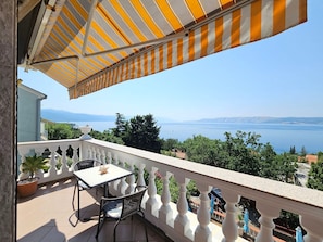 A balcony with a striped awning, a table, and chairs, overlooking a scenic view of a body of water and distant mountains. - Wohnung für 2 Pers. mit Balkon by Interhome (Novi Vinodolski)