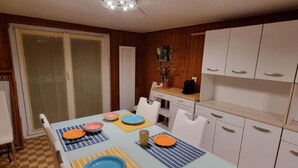 A dining area with a table set for four, white cabinets, and a kitchen area with a coffee machine. - Chez Rosalie by Interhome (La Roche FR)