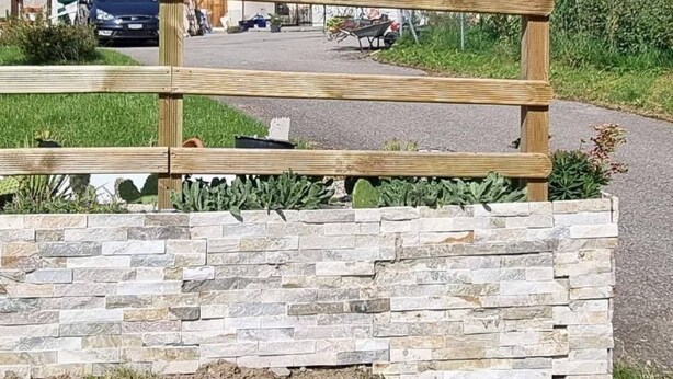 A two-story building with a red-tiled roof and green shutters, a stone wall in the foreground, and a wooden fence. - Chez Rosalie by Interhome (La Roche FR)