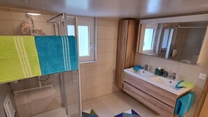 A modern bathroom with a shower, a sink, and a mirror. There are towels hanging on the wall and a rug on the floor. - Chez Rosalie by Interhome (La Roche FR)