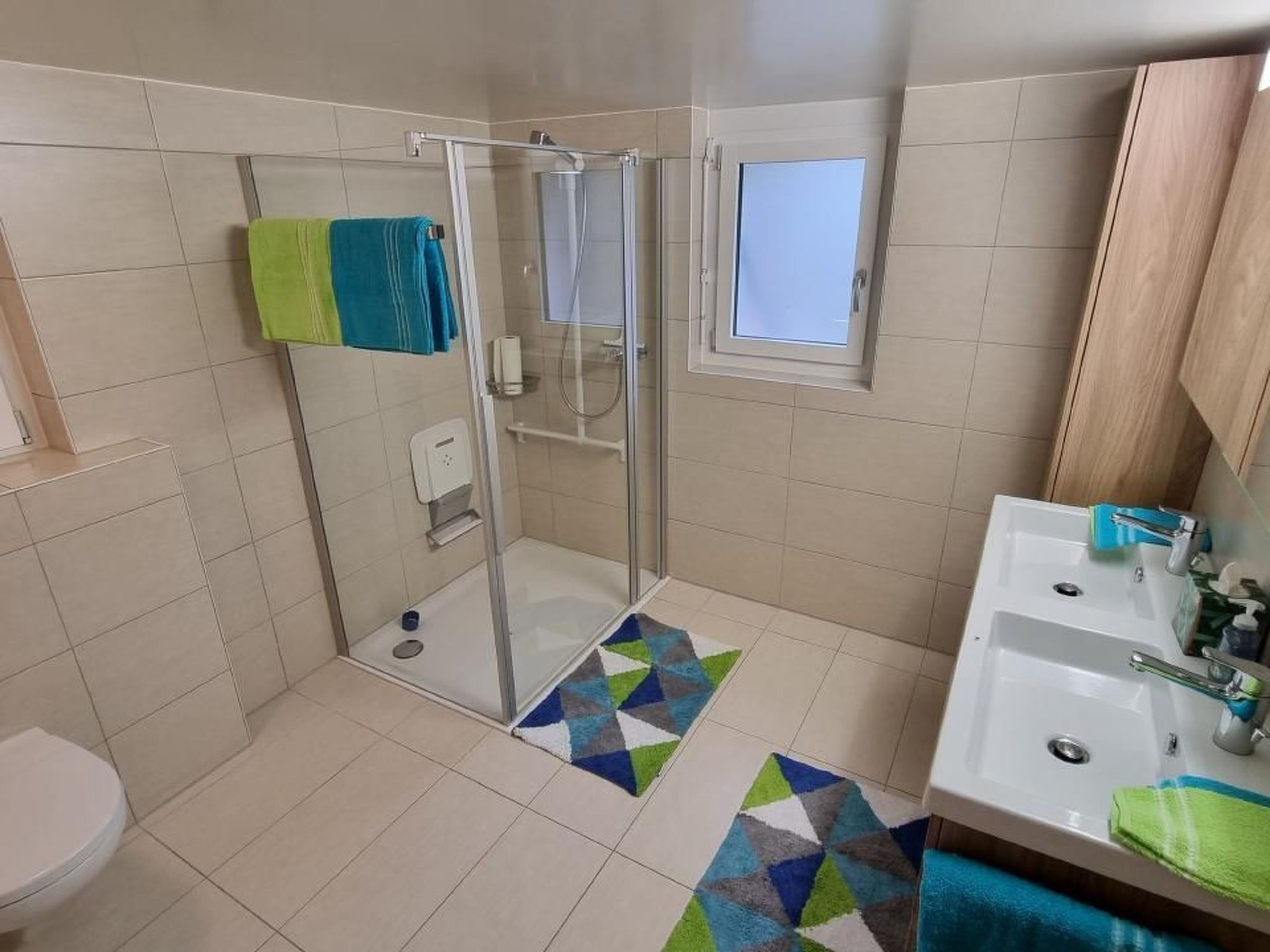 A bathroom with a shower, toilet, sink, and a small window.
